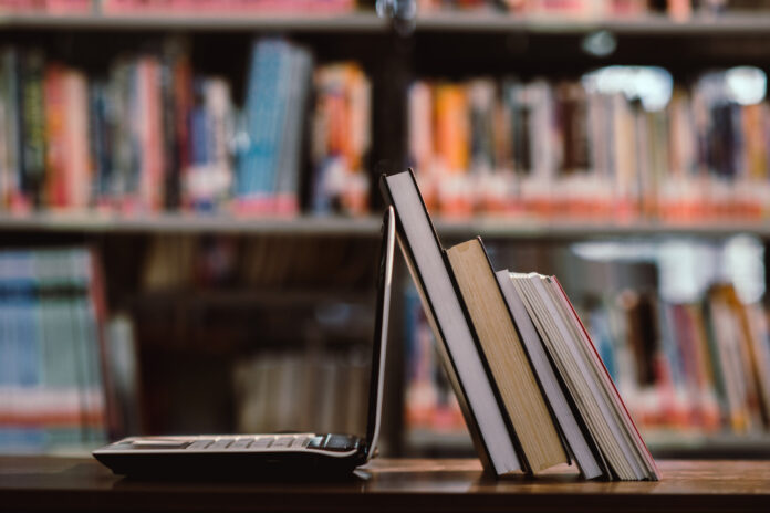 laptop-computer-and-book-on-workplace-in-library-room educazione digitale scuola